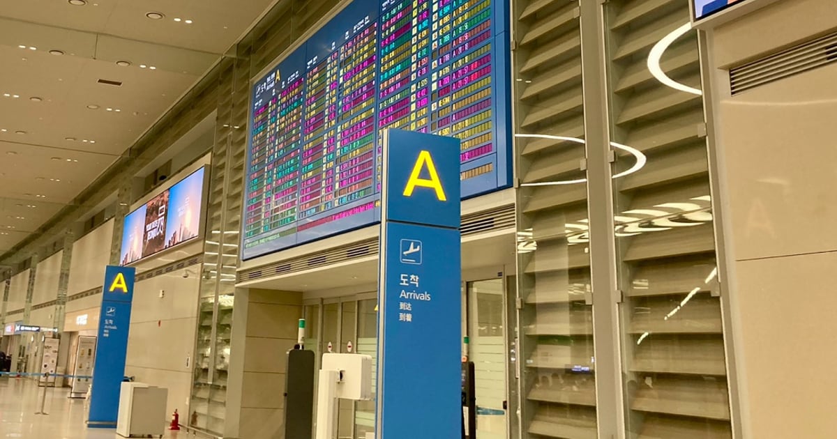 仁川機場第二航廈入境大廳的 A 出口：藍色立柱上有黃色的 A 與「도착 Arrivals 到达 到着」字樣，後方牆上是整面的航班到達資訊看板